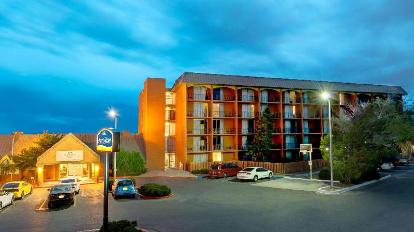A multi-story hotel exterior with illuminated parking lot and parked cars at dusk, featuring a sign with blue and white colors near the entrance.