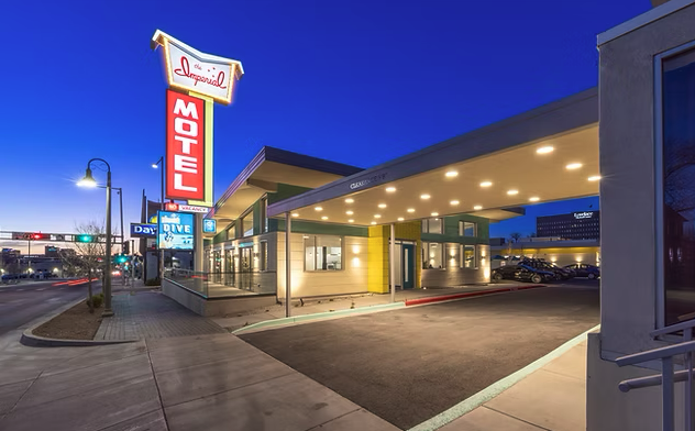 Neon-lit Imperial Motel at dusk, with a retro sign. Empty parking area under bright canopy. Street view includes lampposts and sidewalks.